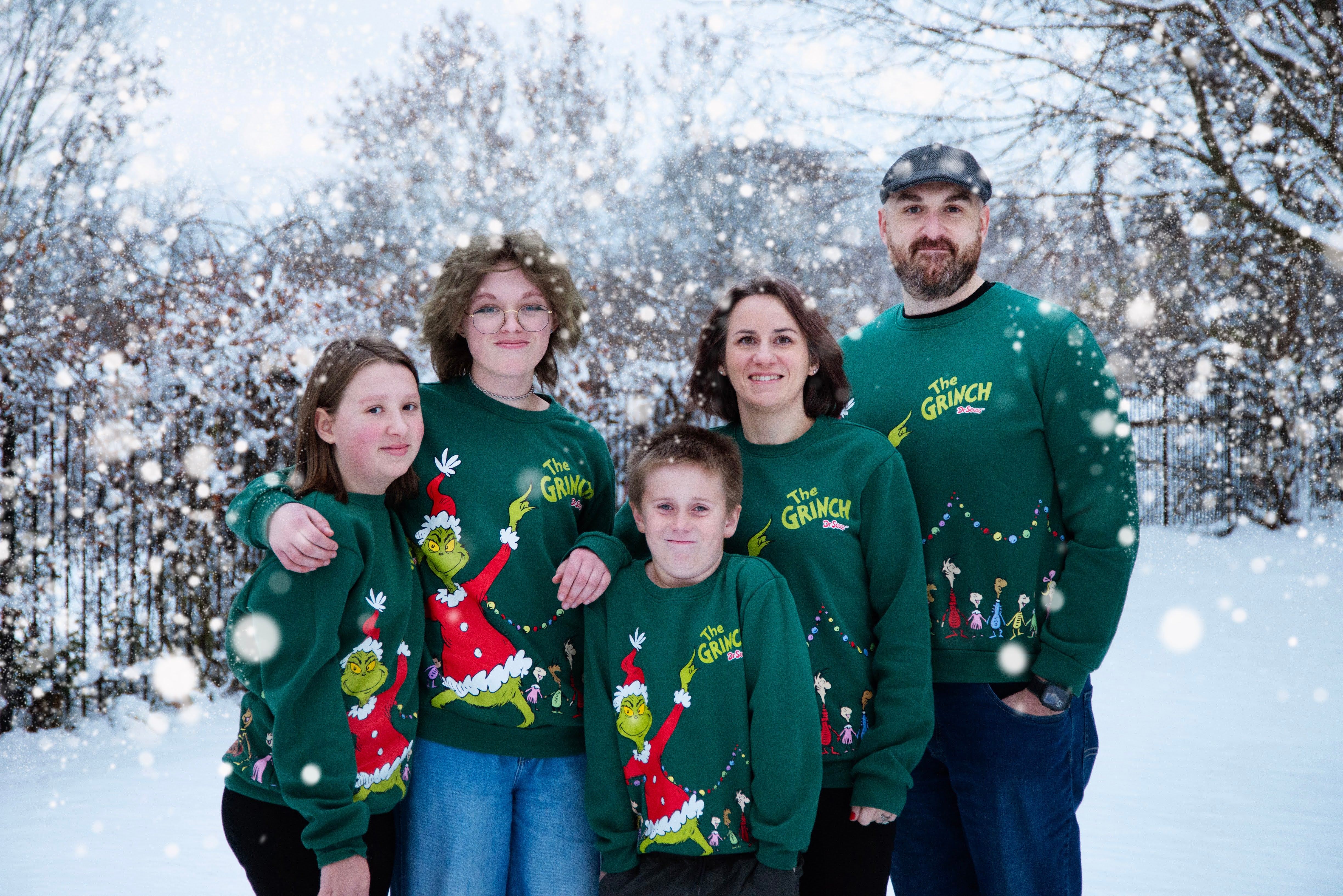 Family wearing Grinch-themed sweaters in a snowy outdoor setting