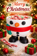 Snowman-shaped mug filled with candy surrounded by Christmas decorations and lights.
