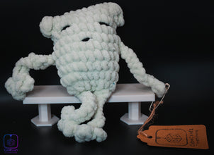 Crocheted frog on a white platform with a brown tag against a dark background