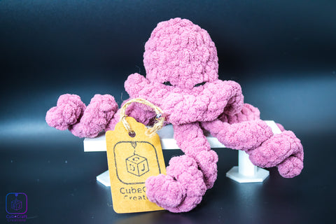 Pink crochet jellyfish toy with a yellow tag on a dark background