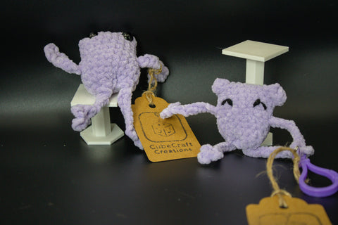 Two purple crochet frog toys with tags on a black background